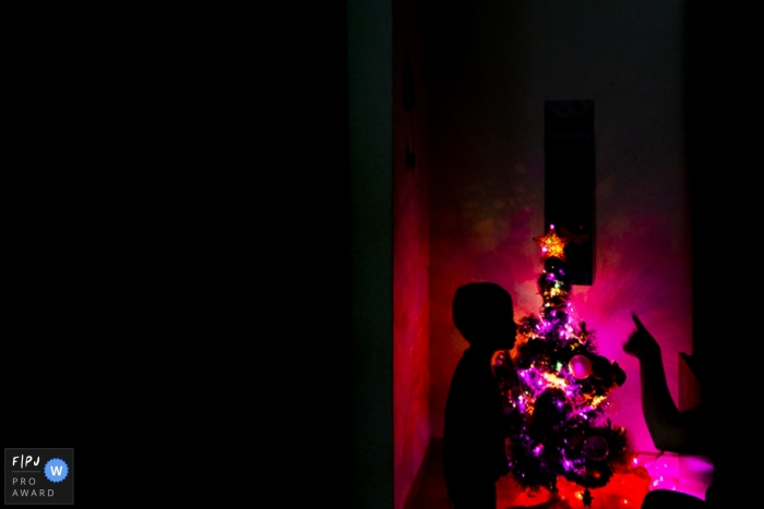 The family turning on the Christmas tree in the dark. The mother is pointing her finger towards the star on the tree to show her son | Arapongas family holiday photographer