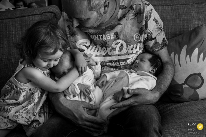 Pendant que papa porte les jumeaux nouveau-nés, sa petite fille fait un gros câlin à l'un des bébés | Photographe de famille Auvergne Rhône Alpes