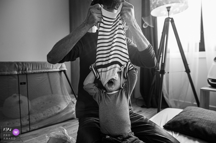 Enfant en bas âge avec sa tête toujours dans son pull que papa décolle. | France famille journée dans la vie photographie