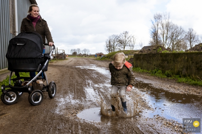 Noord Holland family photo shoot of a mom with stroller watching as her son jumps in puddles.