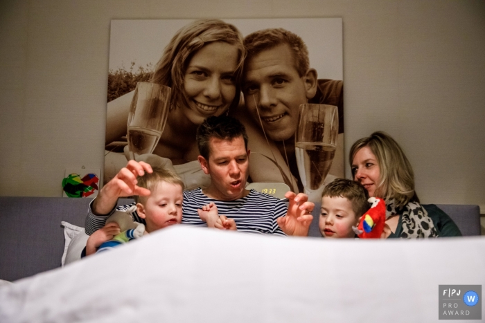 Family sits for a bed time story on a  sofa that displays a portrait of mom and dad on their wedding day | Netherlands family photographer