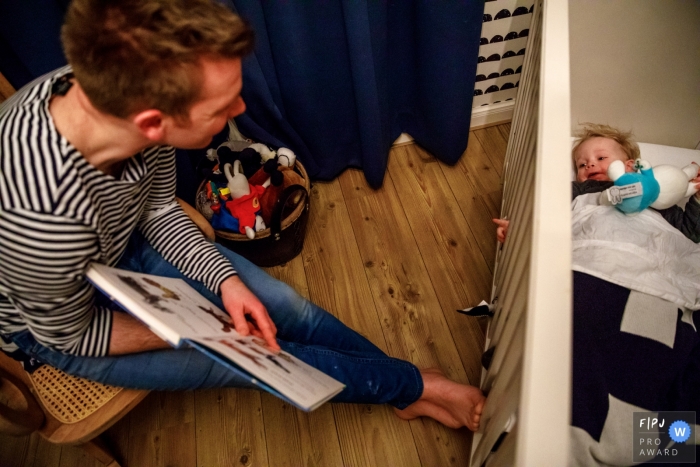 Photo by: <a href="https://www.fpja.com/documentary-family-photography-contests/indra-simons/overijssel/2106174">Indra Simons - Netherlands</a> Bedtime story given to young child in his crib | Overjssel family photography