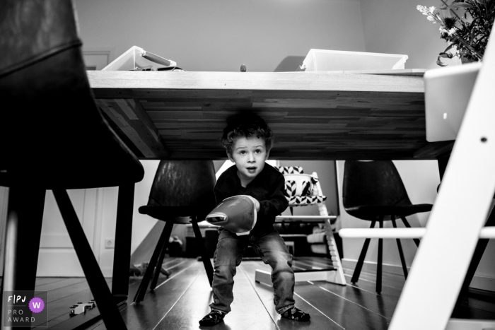 Photo by: <a href="https://www.fpja.com/documentary-family-photography-contests/marieke-zentjens/eindhoven/2106192">Marieke Zentjens - Netherlands</a> Boy helps mom out by using a hand vacuum to do some cleanup under the table | Eindhoven family photography