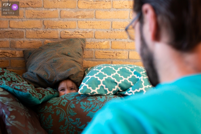 A young child hids amongst pillows, peeking out at dad | Breda Family Photographer