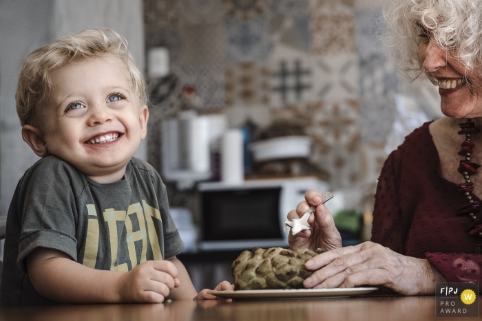 Image captured of a young boy thoroughly enjoying his lunch with grandma by a Rio de Janeiro family photographer Image captured of a young boy thoroughly enjoying his lunch with grandma | Rio de Janeiro family photography