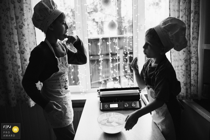 Photo by: <a href="https://www.fpja.com/documentary-family-photography-contests/elena-petrova/saint-petersburg/2106346">Elena Petrova - Russia</a> Kids licking the bowl while cooking with aprons and chef hats during a family photo session in Russia.