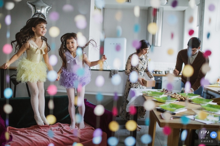 Photo by: <a href="https://www.fpja.com/documentary-family-photography-contests/elena-petrova/saint-petersburg/2106353">Elena Petrova - Russia</a> Birthday party scene of girls jumping in fairy costumes and the parents working at the snack table | Russia Birthday Party Photographer