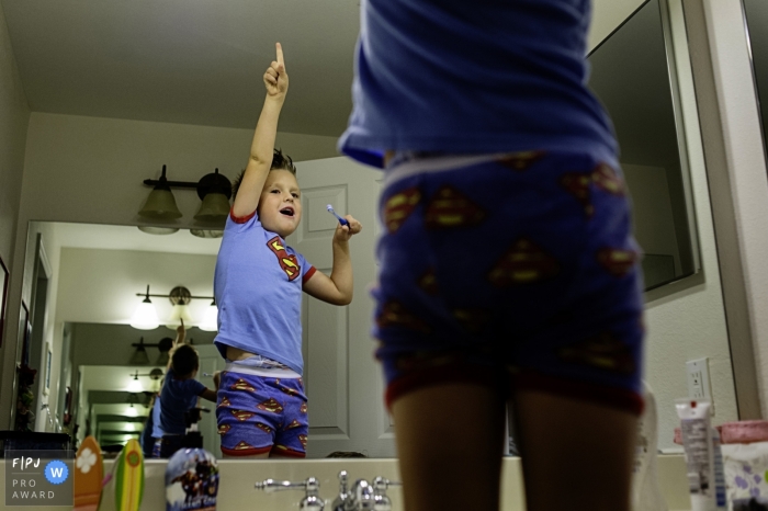Photo by: <a href="https://www.fpja.com/documentary-family-photography-contests/julie-ambos/key-west/2106466">Julie Ambos - United States</a> Boy playing superhero in the mirror while getting ready to brush his teeth | Key West Day in the Life Photographer