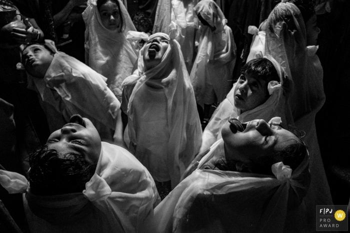 Photo by: <a href="https://www.fpja.com/documentary-family-photography-contests/lisandro-castro/cuiab%C3%A1/2106525">Lisandro Castro - Brazil</a> Several children in coverings looked up as it started to rain at their school theater in Mata Grosso