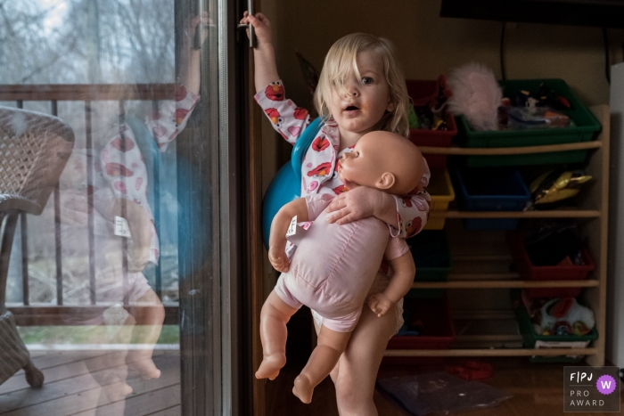 Photo by: <a href="https://www.fpja.com/documentary-family-photography-contests/anna-holden/connecticut/2106595">Anna Holden - United States</a> Image of a young girl with her doll trying to get outdoors at her home in Connecticut.