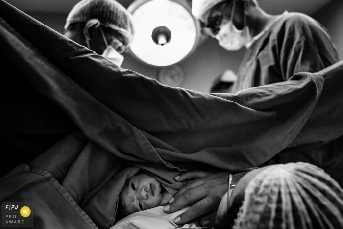 Photo by: <a href="https://www.fpja.com/documentary-family-photography-contests/adriana-costa/belo-horizonte/2107293">Adriana Costa - Brazil</a> Mater Dei Birth Photography | baby in skin-to-skin contact while doctors finish cesarean