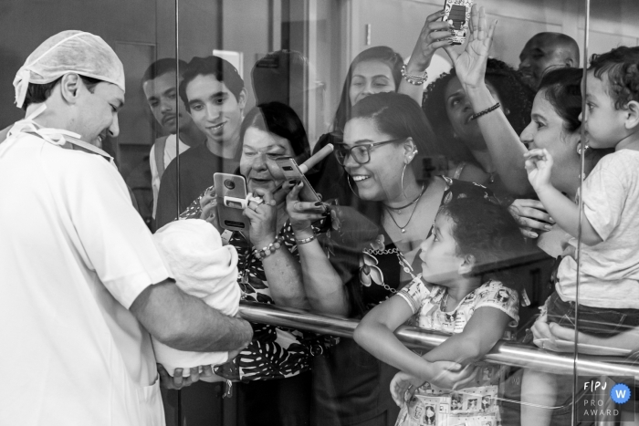 Photo by: <a href="https://www.fpja.com/documentary-family-photography-contests/liliane-cotta/rio-de-janeiro/2107819">Liliane Cotta - Brazil</a> Maternidade Perinatal Family Photo | Father showing the daughter who was just born to the family. It is possible to perceive people's emotion and joy when they see the baby