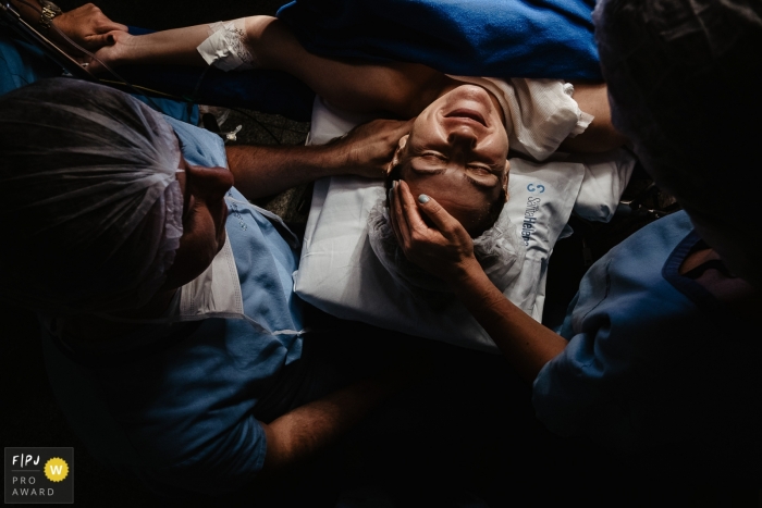 Photo by: <a href="https://www.fpja.com/documentary-family-photography-contests/thiago-braga/florianopolis/2108247">Thiago Braga - Brazil</a> mother with an expression of gratitude and satisfaction, right after the birth of her child. Hand in hand with father and doctor | Maternidade Santa Helena birth photography