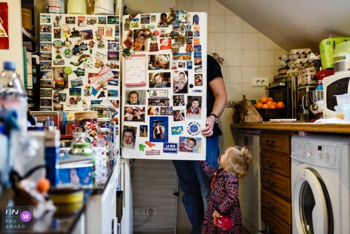 Photo by: <a href="https://www.fpja.com/documentary-family-photography-contests/annie-gozard/paris/2107176">Annie Gozard - France</a> Paris Documentary Family image of the fridgerator door open and a toddler taking a peek