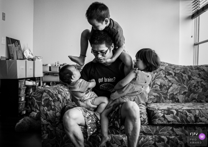 Photo by: <a href="https://www.fpja.com/documentary-family-photography-contests/sherry-tong/chicago/2107324">Sherry Tong - United States</a> Chicago Documentary Family image of dad with his kids sitting and climbing on him