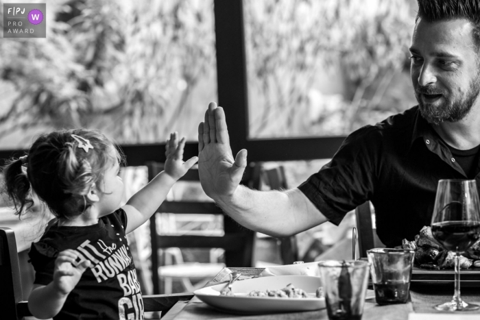 Photo by: <a href="https://www.fpja.com/documentary-family-photography-contests/raluca-chase/essex/2107497">Raluca Chase - United Kingdom</a> Essex Documentary Family Session | little girl giver her dad a high five during a restaurant meal