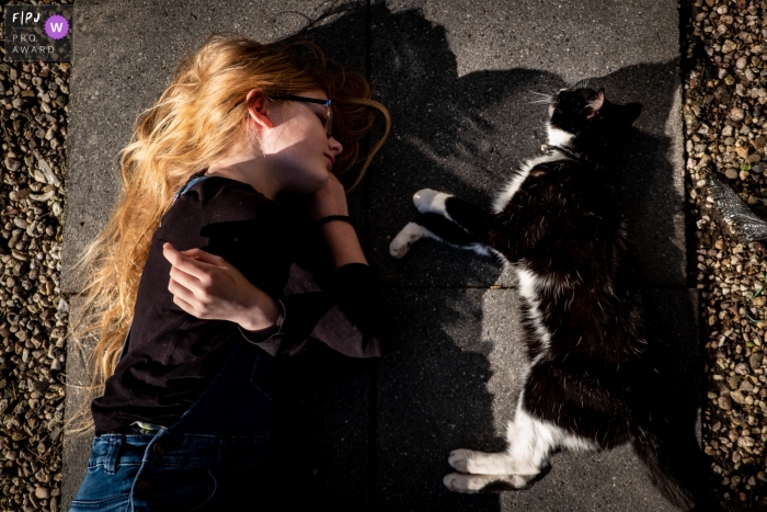 Photo by: <a href="https://www.fpja.com/documentary-family-photography-contests/marjolein-roossien/groningen/2107693">Marjolein Roossien - Netherlands</a> Netherlands Documentary Family photo of a girl and cat lying on the sidewalk