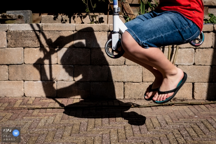 Photo by: <a href="https://www.fpja.com/documentary-family-photography-contests/marjolein-roossien/groningen/2107694">Marjolein Roossien - Netherlands</a> Groningen Documentary Family Photographer | a young boy jumps his scooter and casts his shadow on the brick wall