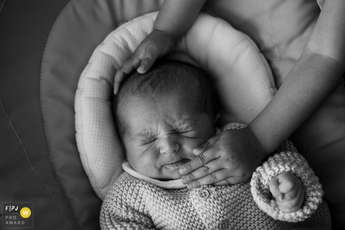 Savoie newborn photography of a baby making a face under the caresses of his big sister Savoie newborn photography of a baby making a face under the caresses of his big sister