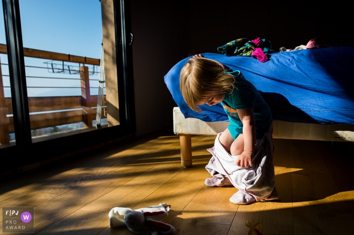 Photo by: <a href="https://www.fpja.com/documentary-family-photography-contests/nadine-court/savoie/2107756">Nadine Court - France</a> Savoie Family photography of a little girl tries to take off her pajamas without help.