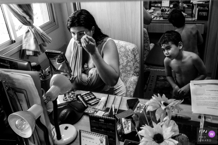 Photo by: <a href="https://www.fpja.com/documentary-family-photography-contests/lisandro-castro/cuiab%C3%A1/2108004">Lisandro Castro - Brazil</a> Cuiaba documentary family photo of a mother nursing, putting on makeup, with her older child nearby