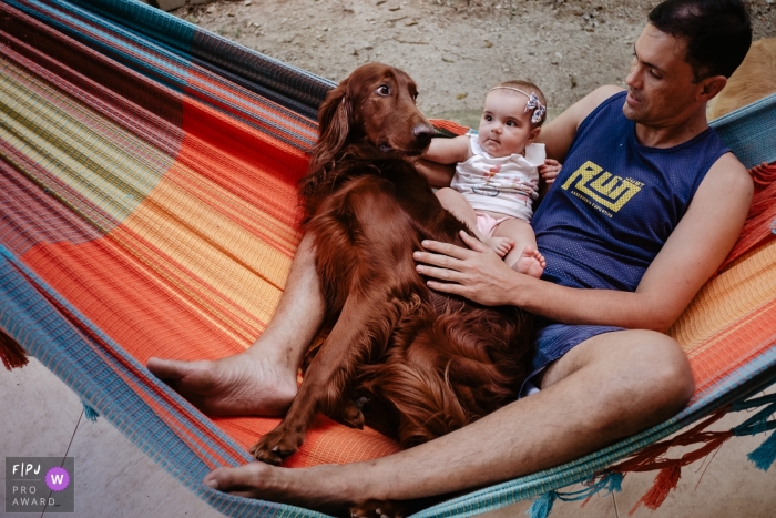 Photo by: <a href="https://www.fpja.com/documentary-family-photography-contests/thiago-braga/florianopolis/2108223">Thiago Braga - Brazil</a> Santa Catarina documentary family image of Father and daughter, in the hammock, with their dog