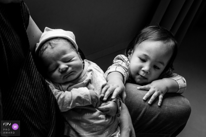Photo by: <a href="https://www.fpja.com/documentary-family-photography-contests/marjolein-roossien/groningen/2108832">Marjolein Roossien - Netherlands</a> NL family photography session at Martini Ziekenhuis Groningen of a young child reaching out to grab the hand of the new baby