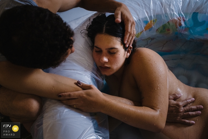 Photo by: <a href="https://www.fpja.com/documentary-family-photography-contests/marcos-paulo/sao-paulo/2110219">Marcos Paulo - Brazil</a> SP, Brazil water birth image shoot in the home with mother in the pool and dad by her side and caring for her