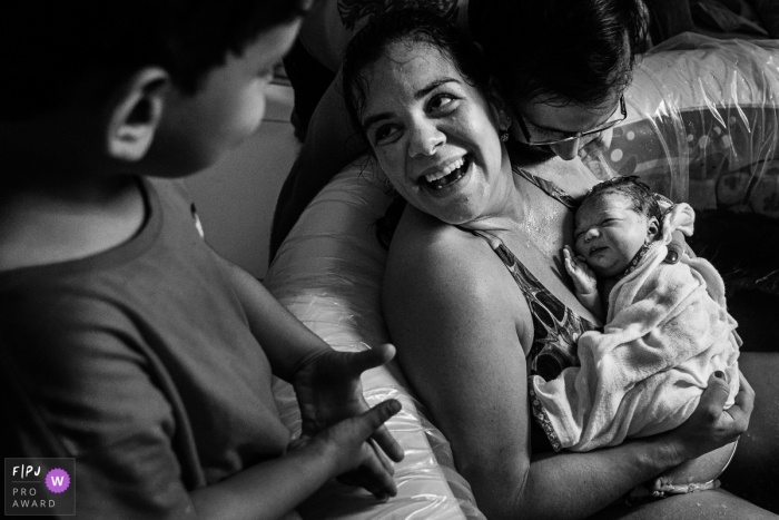 Sao Paulo Family Photographer documents a mother with her newly born baby in her arms while looking up at her older son at this home birth session