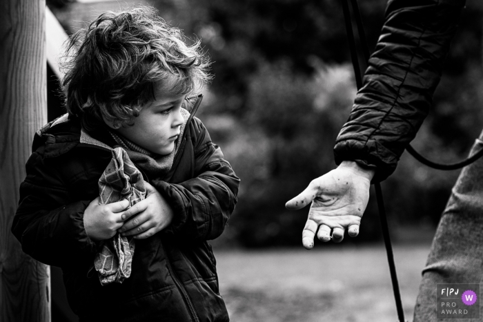 Black and White Wallonie family photos from an outdoor session of child holding back a towel from a reaching parent's hand in Belgium