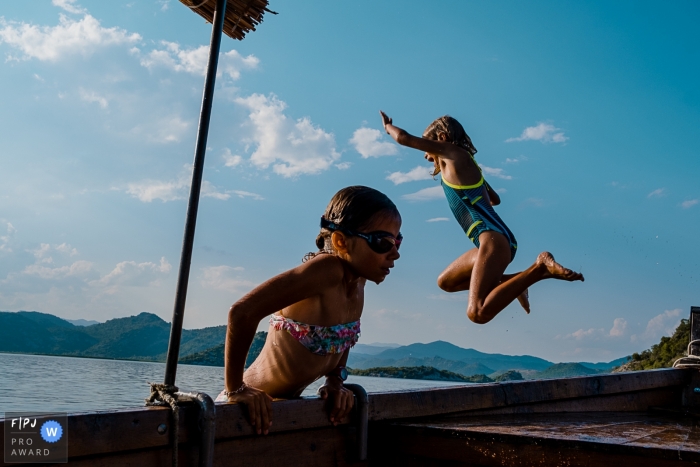Photo by: <a href="https://www.fpja.com/documentary-family-photography-contests/emilie-marchandise/2108603">Emilie Marchandise - Belgium</a> Wallonie family photography session at the water of girl jumping from a dock and one girl climbing out