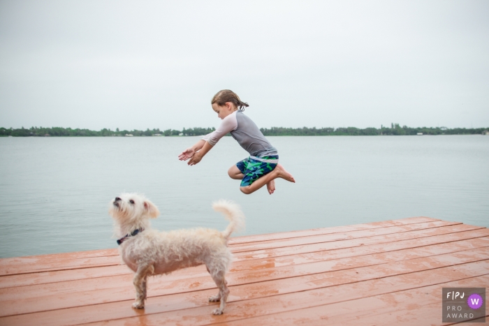 Sarasota Florida family photo of A young boy bravely jumping from the deck of his family lake house with his dog looking on Sarasota Florida family photo of A young boy bravely jumping from the deck of his family lake house with his dog looking on