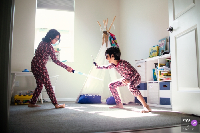 Photo by: <a href="https://www.fpja.com/documentary-family-photography-contests/samantha-moore/sarasota/2108620">Samantha Moore - United States</a> Florida Brothers have a sword fight in their playroom while mom is asking them to go upstairs and get dressed for their day in this Sarasota family photography