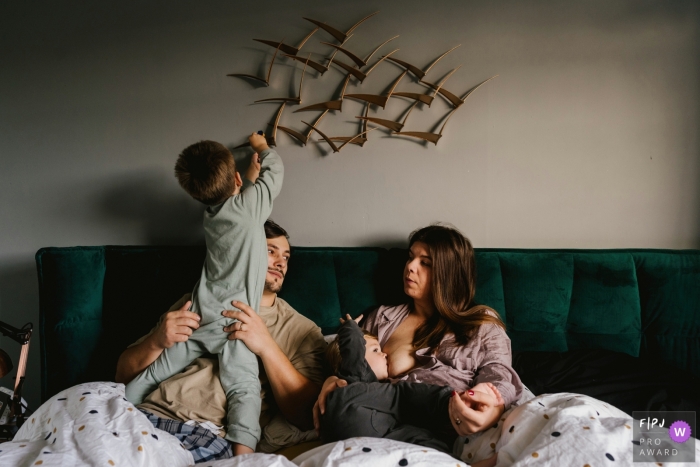 Photo by: <a href="https://www.fpja.com/documentary-family-photography-contests/sharron-gibson/bedfordshire/2108714">Sharron Gibson - United Kingdom</a> Bedfordshire Boy climbing on dad while mum breastfeeds in this at-home England family photo session