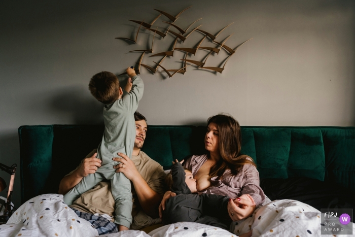 Bedfordshire Boy climbing on dad while mum breastfeeds in this at-home England family photo session