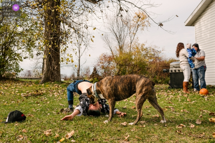 Photo by: <a href="https://www.fpja.com/documentary-family-photography-contests/viara-mileva/kingston/2108728">Viara Mileva - Canada</a> Ontario boy and dog play in the back yard while everyone is busy with the baby in this Kingston family photography