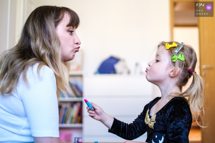 Photo by: <a href="https://www.fpja.com/documentary-family-photography-contests/jess-haverkamp/berlin/2108760">Jess Haverkamp - Germany</a> Germany documentary-style family photography session of girl preparing mom to receive some lipstick