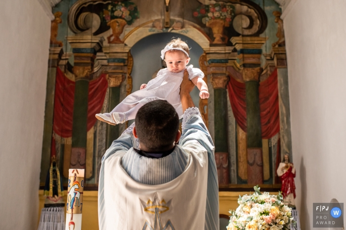 RJ baby baptism photographer captures a young girl being lifted by a priest in Niterói