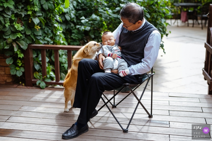 Shanxi outdoor family photography session in the home garden of a baby being held with a very curious dog in China Shanxi outdoor family photography session in the home garden of a baby being held with a very curious dog in China
