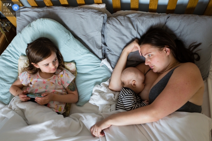 Photo by: <a href="https://www.fpja.com/documentary-family-photography-contests/rose-dedman/bath/2108963">Rose Dedman - United Kingdom</a> Bath family photography session in the home documenting a resigned, tired mother looking at her eldest in bed whilst feeding her youngest