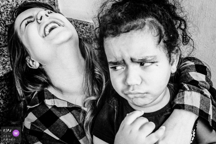 Photo by: <a href="https://www.fpja.com/documentary-family-photography-contests/thiago-gimenes/sao-paulo/2108968">Thiago Gimenes - Brazil</a> SP, Brazil family photographer captures a mother in laughter as her daughter if expressing opposite feelings