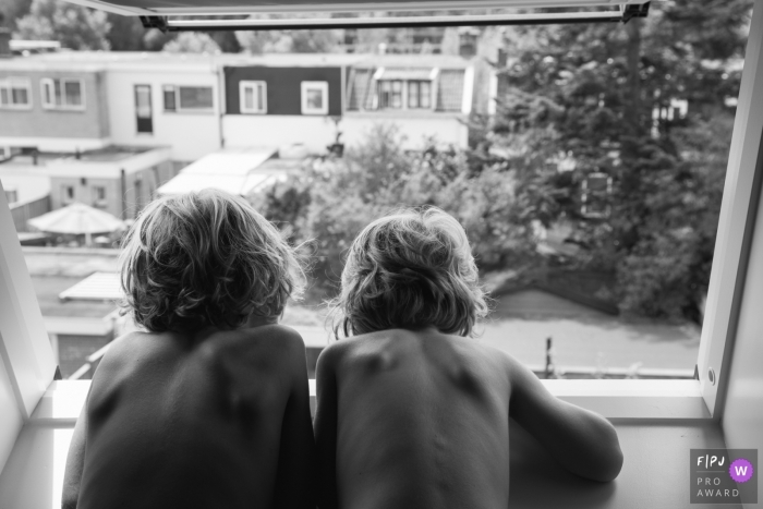 Photo by: <a href="https://www.fpja.com/documentary-family-photography-contests/sjors-van-gils/s-hertogenbosch/2109095">Sjors van Gils - Netherlands</a> NB black and white family photography capturing two brothers plotting their plan on how to spray their neighbours with their water pistols without getting spotted. Discussing the best positions for maximum impact!