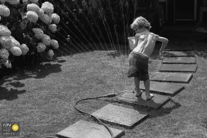 NB funny family pictures from an at-home photo session by Netherlands Photographer: "The sprinkler is turned on and everyone is running up and down the garden avoiding the cold beams! except for one: “come on, what are you waiting for?"