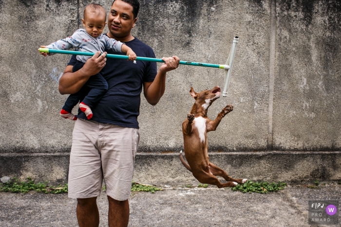 MG outdoor family image session from the home of a dog trying to get the squeegee that the child's father used to clean the yard in Brazil