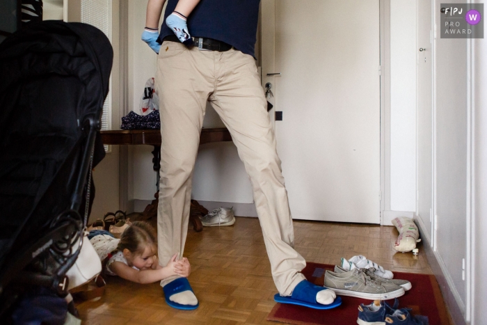 Photo by: <a href="https://www.fpja.com/documentary-family-photography-contests/annie-gozard/paris/2109149">Annie Gozard - France</a> Paris, FR documentary-style family photography session of a young girl slides across the floor holding tight to her father's leg