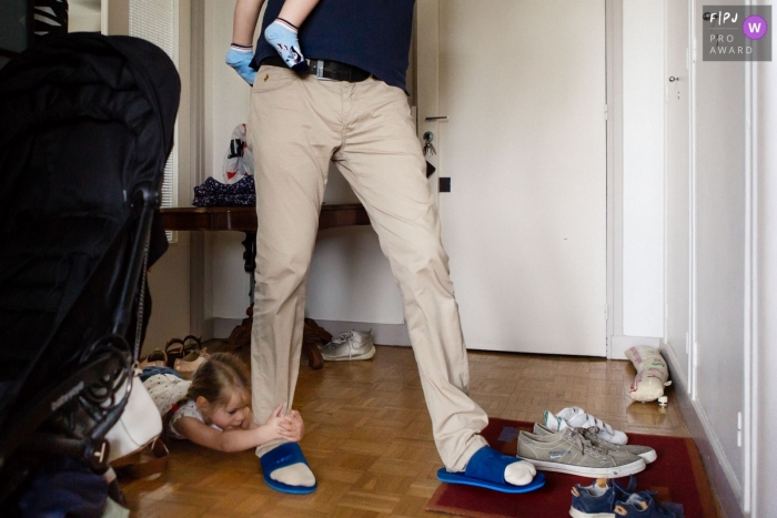 Paris, FR documentary-style family photography session of a young girl slides across the floor holding tight to her father's leg