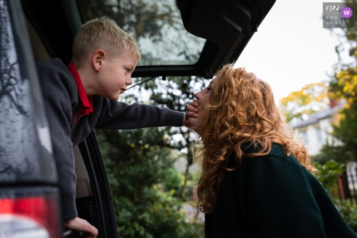Photo by: <a href="https://www.fpja.com/documentary-family-photography-contests/alice-chapman/cambridgeshire/2109472">Alice Chapman - United Kingdom</a> Cambridgeshire Family Photo of a young boy reaching out the back of a car while covering his mum's mouth