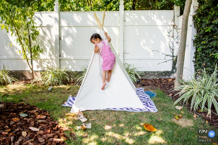 Young girl is documented by a San Francisco Photographer of her climbing up the side a teepee in her backyard camp