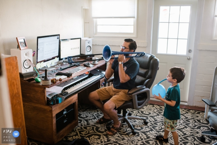 Photo by: <a href="https://www.fpja.com/documentary-family-photography-contests/tiffany-luong/los-angeles/2110280">Tiffany Luong - United States</a> Los Angeles Family Photographer creates this image of a father teaching music class working from home while his son blows up a balloon