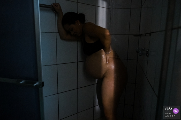 Photo by: <a href="https://www.fpja.com/documentary-family-photography-contests/lisandro-castro/cuiab%C3%A1/2111391">Lisandro Castro - Brazil</a> Maternidade Femina hospital natural birth photo showing A light finds the mother calming the pain of contraction in the shower